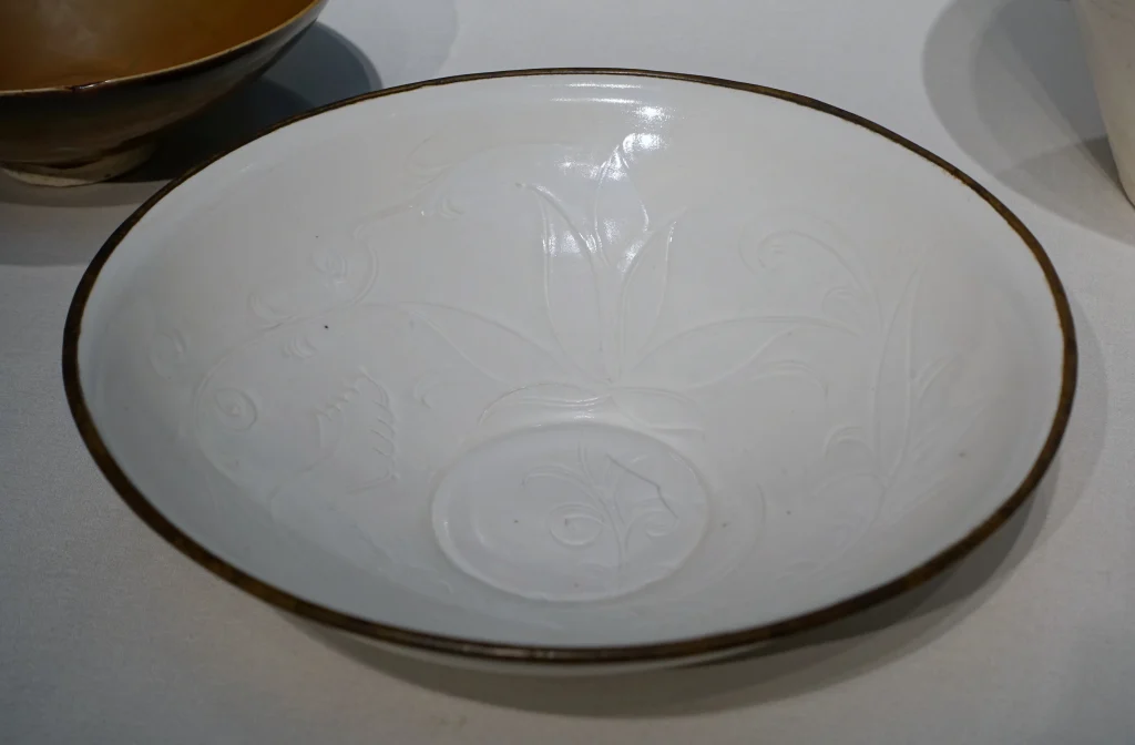 Northern Song Ding ware dish with incised lotus, attributed to the Quyang Ding kilns, photographed in a museum display