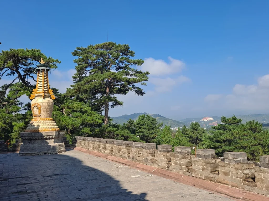 Glazed stupa beside the stone terrace at Pule Temple with wooded Chengde hills beyond