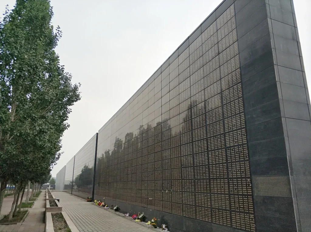 Long dark memorial wall engraved with names at Tangshan Earthquake Memorial Park, with flowers placed along its base